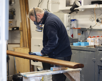 A handrail being stained by a Maintenance man. He is wearing a face mask with a filter. 