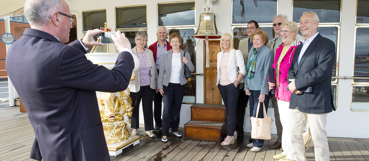 A visitor assistant taking a photo of a groups of visitors by Britannia's bell. 