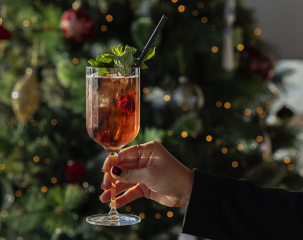 A hand is holding a cocktail in front of a Christmas tree on Britannia. 