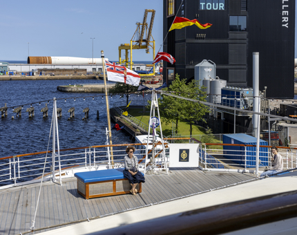 A woman sitting on a box on the Verandah Deck at Britannia enjoying the sunshine. 