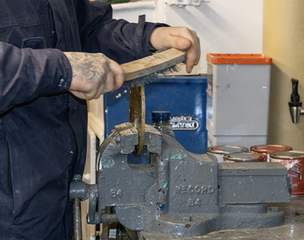 A maintenance team member holding a wire brush to clean a lid from a fuel tank aboard the Admiral's Fast Motor Launch. 