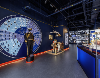 Inside the brand new Visitor Centre at Britannia. The Admiral's uniform is displayed in front of a wall display of a wheel that details all of the different job roles aboard. To the right is a model of Britannia and in the background is a cascading wall of images and video. 