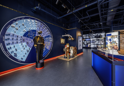 Inside the brand new Visitor Centre at Britannia. The Admiral's uniform is displayed in front of a wall display of a wheel that details all of the different job roles aboard. To the right is a model of Britannia and in the background is a cascading wall of images and video. 