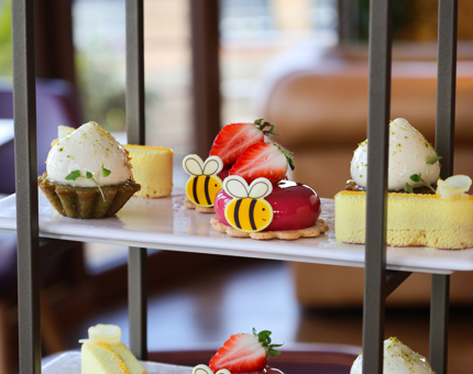 A close look at The Lighthouse Restaurant's Easter afternoon tea sweet selection on a cake stand. There are small edible bee decorations. 