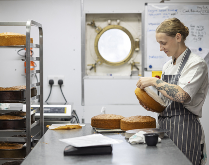 A Chef in the Galley taking cakes out of their pans. 
