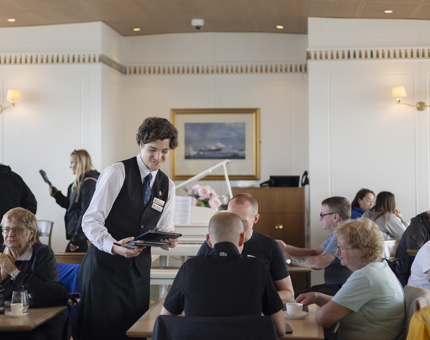 A Hospitality Server in the Royal Deck Tearoom is taking a food and drinks order from a guest.
