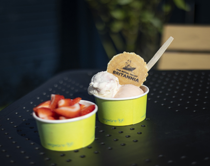 A pot of strawberries and a pot of ice cream with a wafer are sitting on a table. 