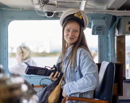 A woman sitting in the Captain's chair in Britannia's Bridge in Edinburgh, she is wearing a Captain's hat.