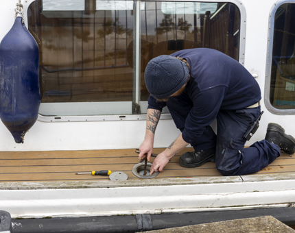 A man kneeling on a boat, putting fuel into it. 