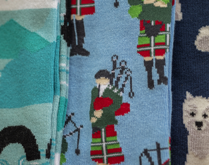 A close up of 3 pairs of Scottish themed socks one has a bagpiper another has scotty dogs.