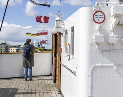 A person is standing by the railing, taking a picture of colourful dress flags flying above Britannia's Bridge. 