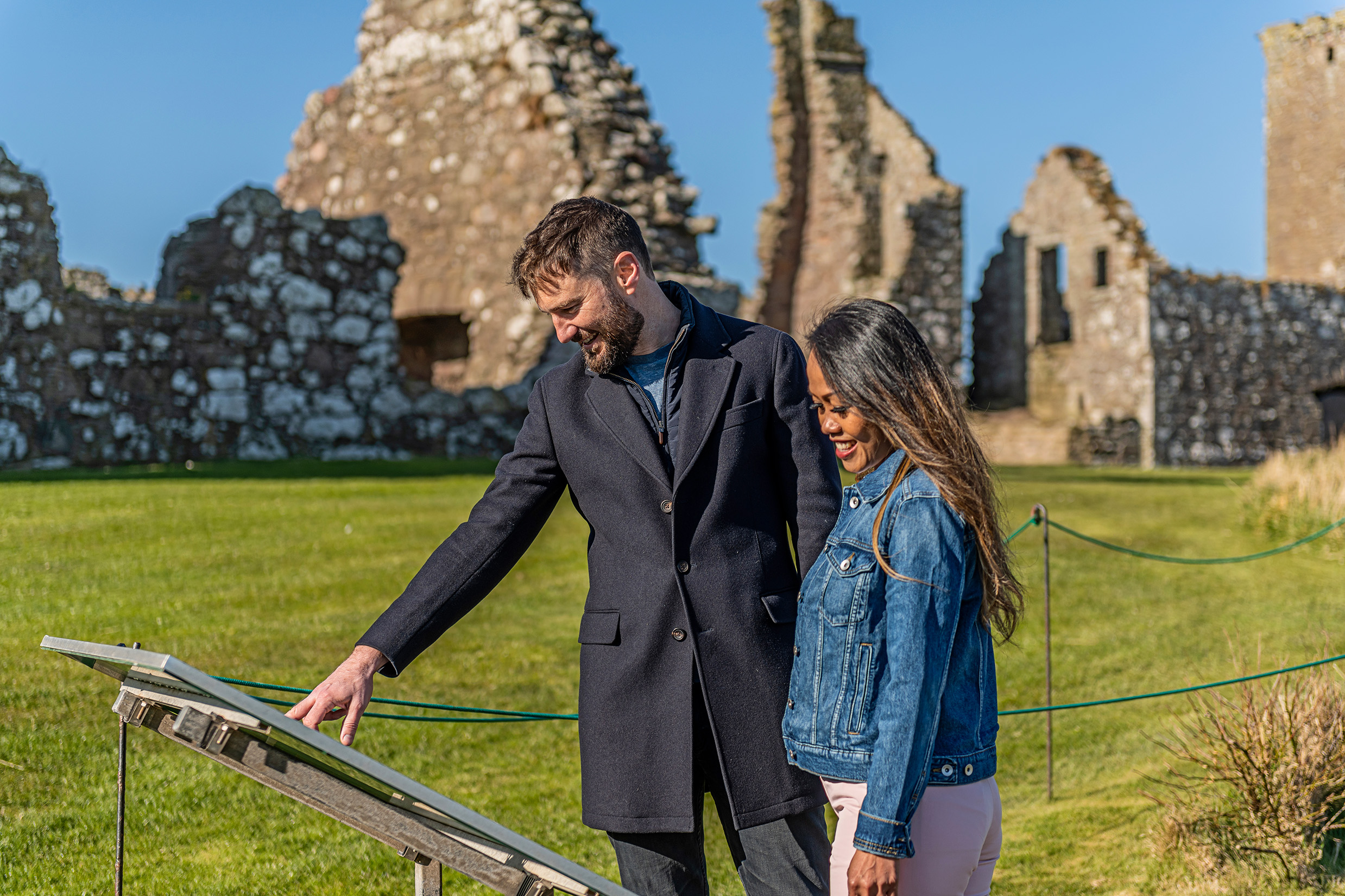 A man and woman looking at a sign at Dunnottar Castle in Scotland.