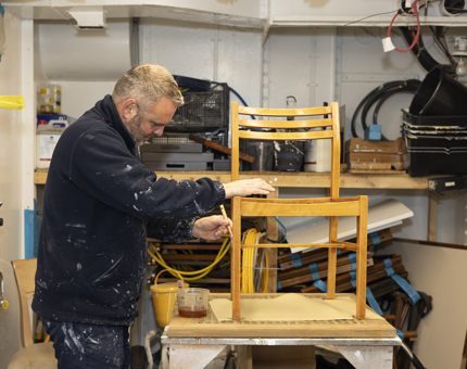 In the Joiner's Workshop, a Maintenance team member is varnishing a chair from the CPOs Mess. 