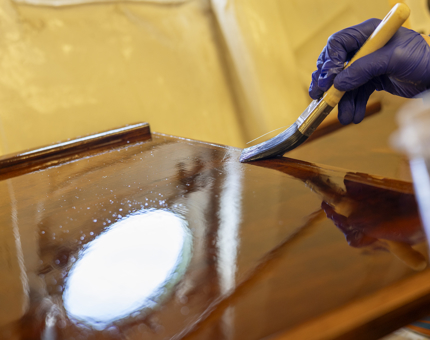 A close up of varnish being applied to a wood panel. 