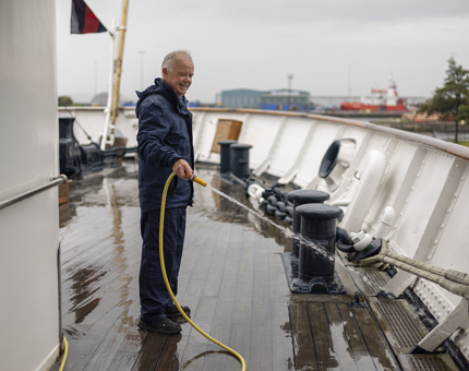 A Maintenance team member on Britannia holding a hose, washing down the deck.