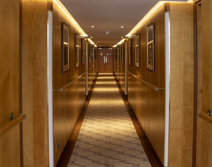 A hallway aboard Fingal Hotel with doors leading to their cabins along the way. There are photographs of lighthouses adorning the wall. 