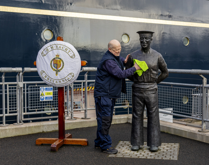 A man is cleaning a statue of a Yachtsman on the quayside next to Britannia. 