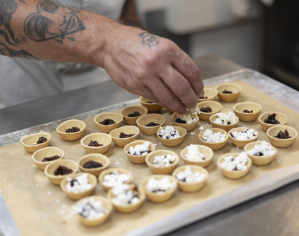 A tray of capapes is being made. A Chef is filling pastry cases with goats' cheese.