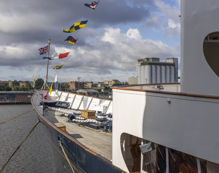The bow of Britannia looking out over the Port of Leith. There are colourful flags flying over the ship. 