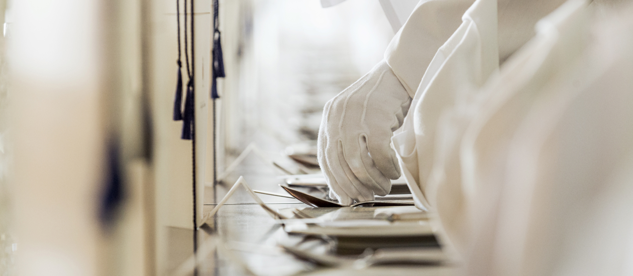 A close up of a white gloved hand setting a table. 