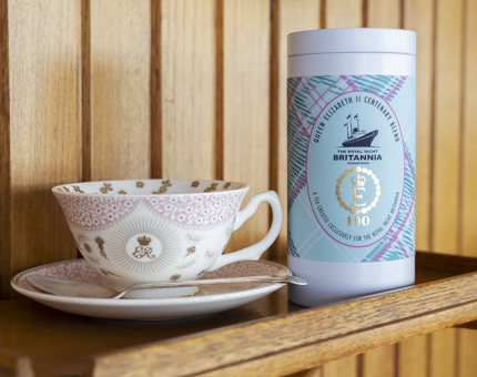 A cup and saucer commemorating 100 years since Queen Elizabeth II's birth and a tin of tea wrapped in a tartan label. 