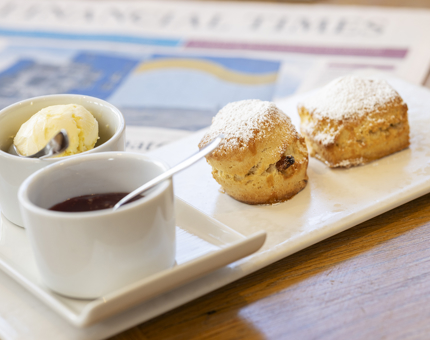 A plate with two scones and a pot of jam and cream on it. 