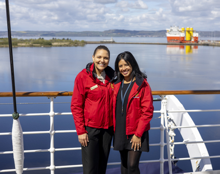 Two women wearing red jackets are smiling on The Bridge. 