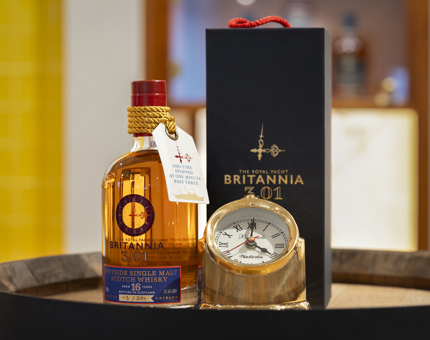 A bottle of 301 whisky sitting on the top of a barrel, there is a packaging box and a small nautical clock.