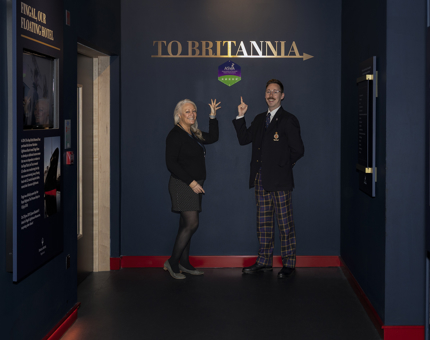 Two members of Britannia staff are posing in front of a small ASVA sign in Britannia's Visitor Centre. 
