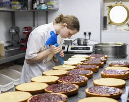 In the Galley, a chef is piping icing onto Victoria sponge cakes lined up on the bench. 
