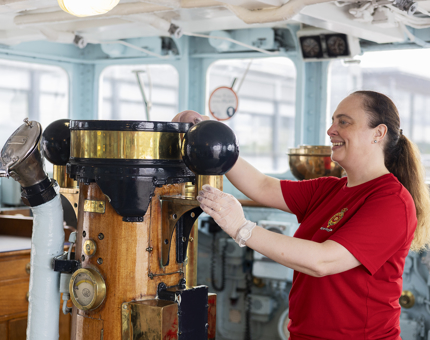 A Housekeeper is in the Bridge polishing the brass. 