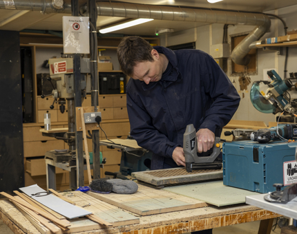 In the workshop, a Maintenance man is reinforcing scupper boards. 