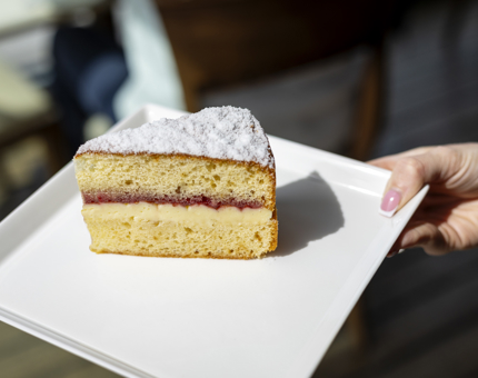 A hand holding a slice of Victoria sponge cake.
