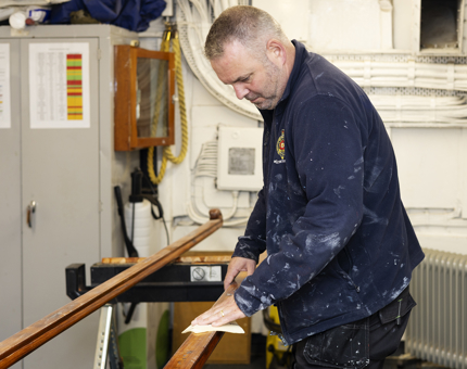  A Maintenance man is Sanding Handrails In Preparation For Varnishing. 
