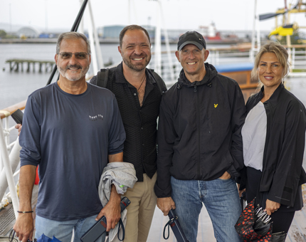 Four people pose for a photo on Britannia's Verandah Deck. The Port of Leith is in the background. 
