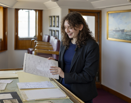 The Archivist is in the Chartroom aboard Britannia, they are looking through folders of documents. 