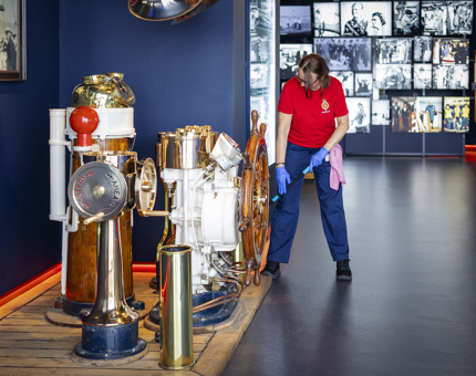 A Housekeeper is sweeping by the ship's wheel in the Visitor Centre in Leith. 