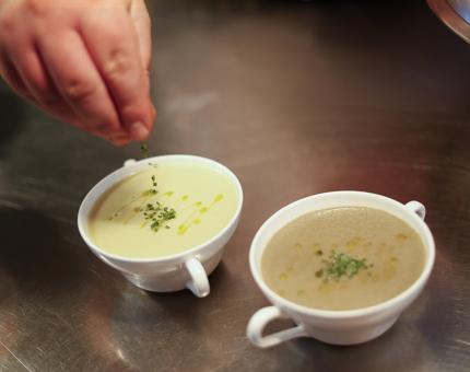A hand is sprinkling chives onto two bowls of soup in the Tearoom's Galley.
