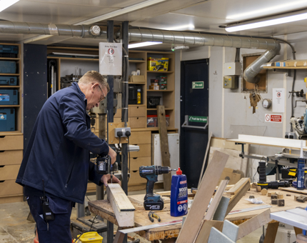 A maintenance team member in the joiners workshop drilling into a piece of wood.