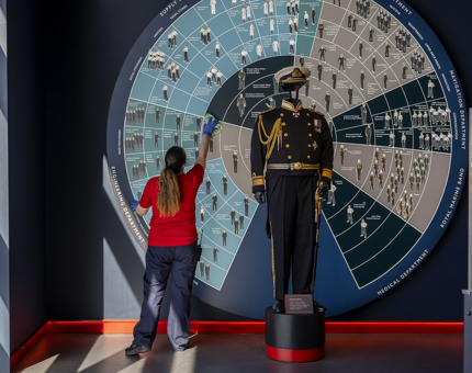 A Housekeeper is wiping the wall behind a mannequin wearing a naval uniform in Britannia's Visitor Centre in Leith. 