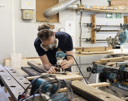 A maintenance man at a work bench cutting wood. 