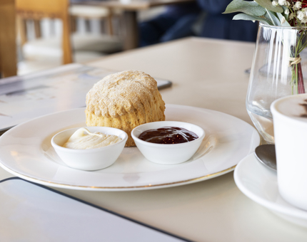 A scone on a plate with small pots of jam and cream. 