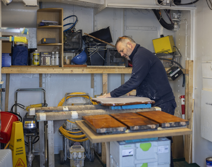 A maintenance man sanding the crest that hangs above Britannia's Bell on the Verandah Deck. 