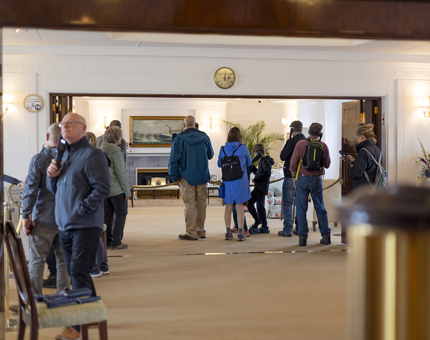 Visitors touring the Drawing Room Anteroom and Drawing Room aboard The Royal Yacht Britannia in Edinburgh, listening to their audio guide handsets.