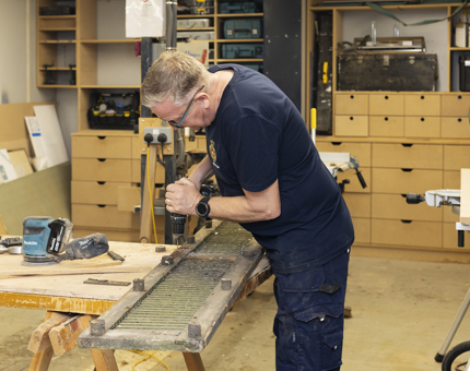 A Maintenance man is in the workshop repairing scupper boards. 