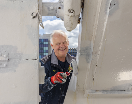 A maintenance team member holding a paint roller painting the port side of Britannia white. 