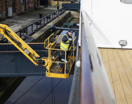 A man is on a yellow cherry picker painting the side of Fingal Hotel in the Port of Leith. 