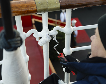 A close look at a Maintenance team member using a small paint roller to apply a coat of white paint the the railings. 