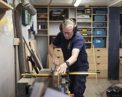 A Maintenance man is planing a scupper board facing in the workshop. 