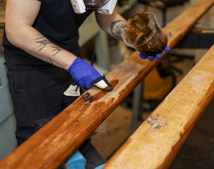 A close up of hands holding a pot of varnish and a paint brush to varnish wooden handrails.